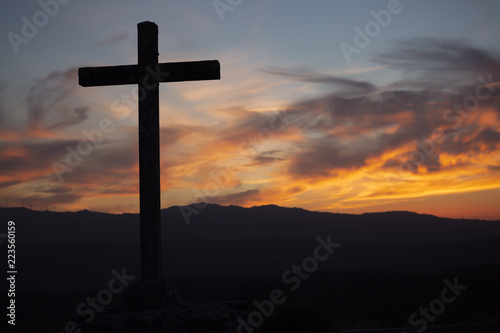 Religion theme, view of catholic cross in black shadow, with fantastic sunset with warm colors and mountains as background, in Viseu, Portugal