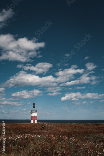 A girl and a lonely red-white lighthouse in an autumn field on the shores of the Okhotsk Sea in the north of the Khabarovsk Territory of Russia