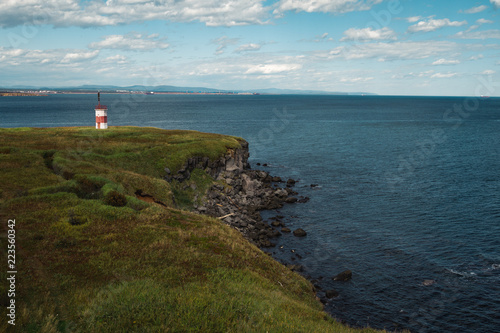 Insanely beautiful red and white lighthouse on the rocks on the shores of the Okhotsk Sea in the north of the Khabarovsk Territory of Russia. Beautiful lighthouse