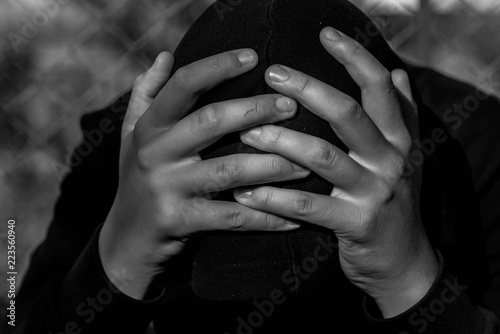 Young unidentifiable teenage boy  holding hes head at the correctional institute in black and white, conceptual image of juvenile delinquency, focus on the boys hand.