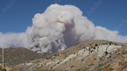 Timelapse-Clouds of billowing smoke churn over hills and red rock cliffs against a clear blue sky as the Pole Creek fire in the Uinta-Wasatch-Cache National Forest in central Utah burns out of control