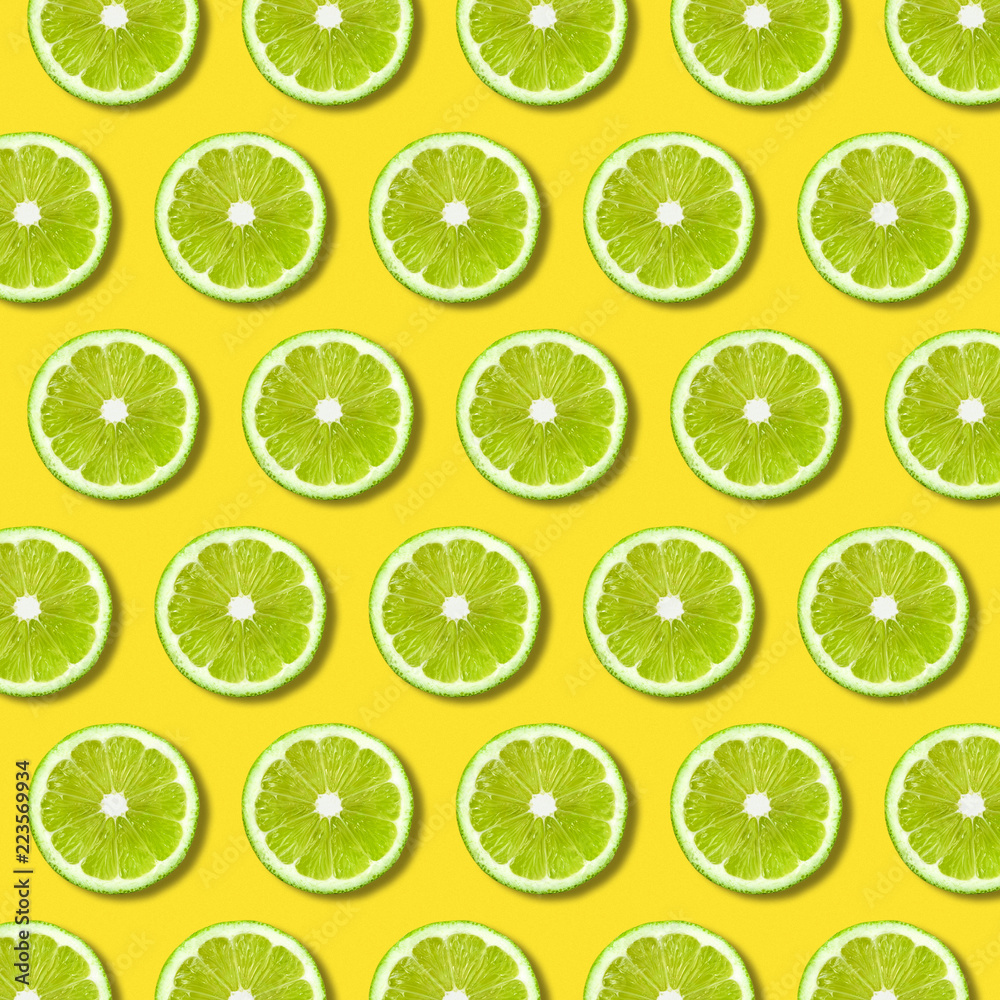 Green lime slices pattern on vibrant yellow color background. Minimal flat lay food texture 