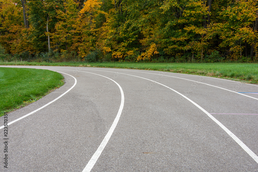 Obraz premium vacant sports track with white lines curving into autumn trees