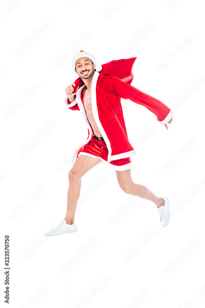 happy muscular man in santa claus costume jumping with christmas sack isolated on white background