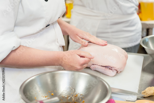 A culinary student prepares a raw duck for cooking.