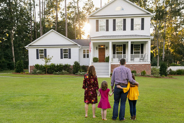 Family of Four With Daughters Looking at Their New Construction White Farmhouse Home