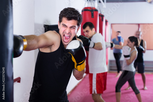 Muscular man is beating a boxing bag © JackF