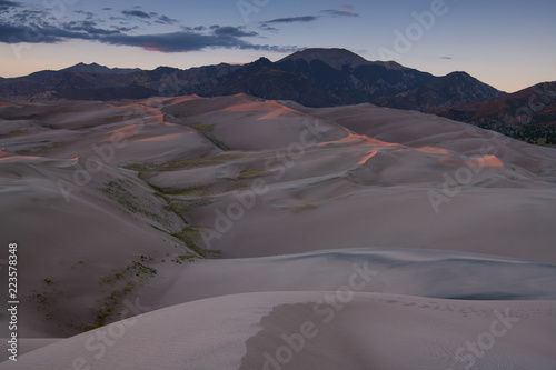 Vast landscape of dunes topped with rosy sunset light in Great Sand Dunes National Park, backed by the Rocky Mountains