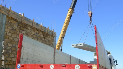 The mobile crane lifts the concrete slab next to the unfinished building