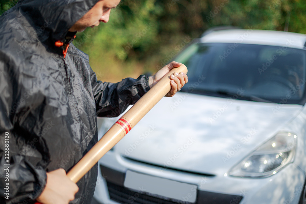The aggressive person with the baseball bat in front of the car The aggressive person with the baseball bat in front of the car