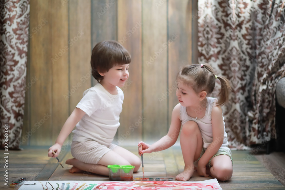 Little children paint on a large sheet of paper