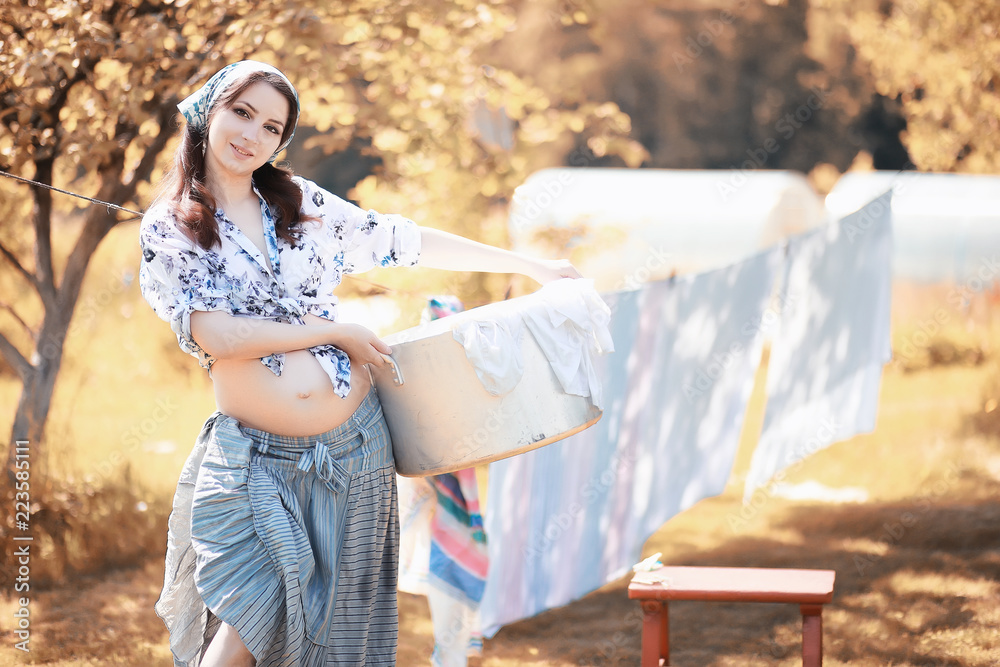 Naklejka premium Pregnant woman hanging sheets on the rope for drying