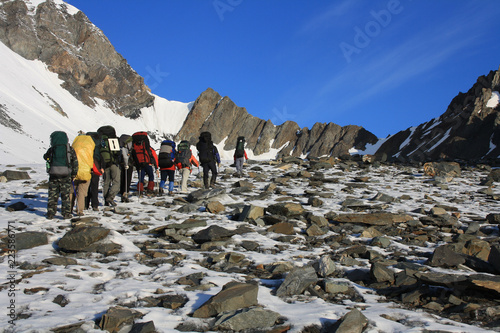 Backs of group of climbers walking along the glacier to conquer the mountain pass on a sunny morning. Altai, Russia.