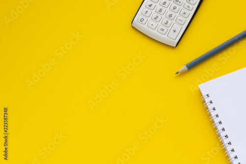 Calculator, notepad and pencil on a yellow background, space for text