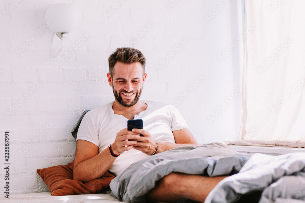 Young man using smartphone in the bed in the morning Young man using smartphone in the bed in the morning