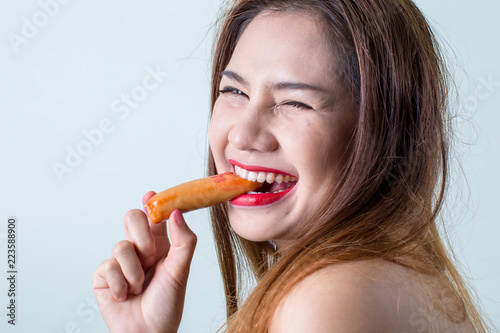 Young woman eating sausage or hotdog.  girl is sitting in the kitchen and greedily eats sausage. women eating sausage with hand lifestyle shot. girl eating meat sausage in the backyard