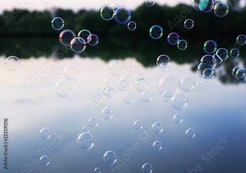shiny iridescent soap bubbles flying over a quiet evening by the pond at sunset