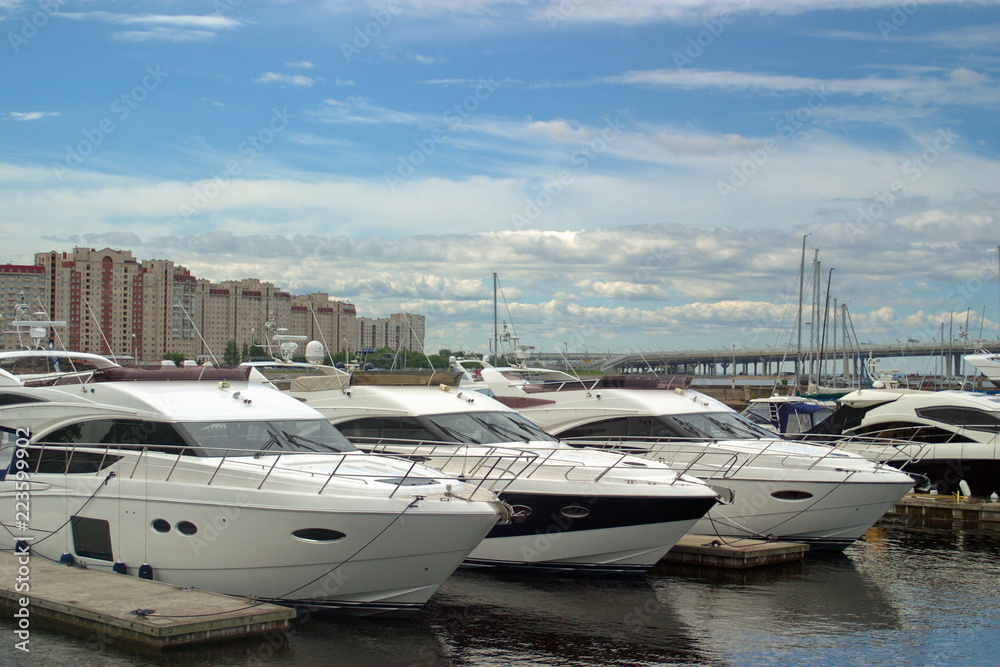 Fototapeta premium Motor yachts are moored in the Harbor of the yacht club on the Malaya Nevka river. Saint-Petersburg. Against the background of residential neighborhoods.