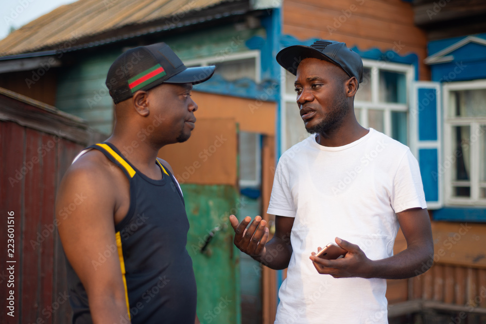 Two black guys discuss business issues on background of a village house