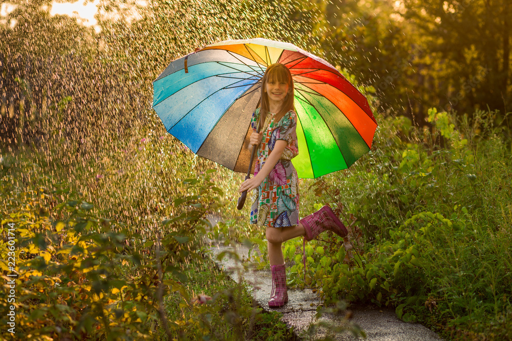 Happy child girl walk with multicolored umbrella under summer rain 