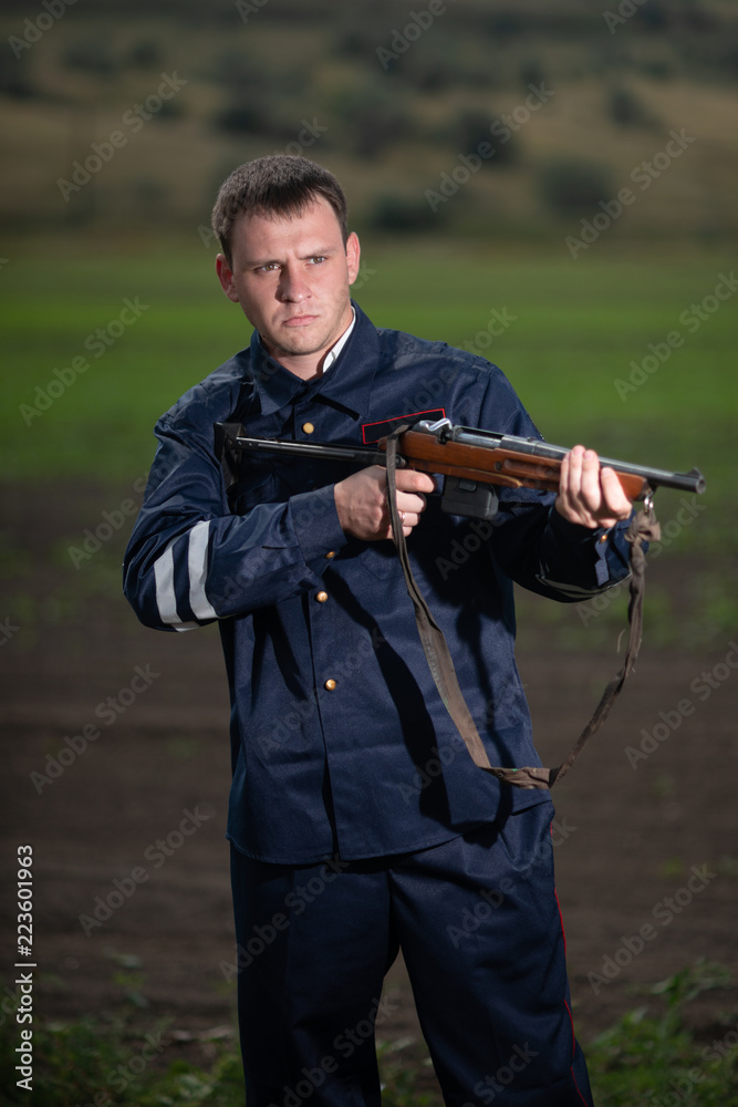 Young police officer in uniform, with weapon in hand on rural landscape background