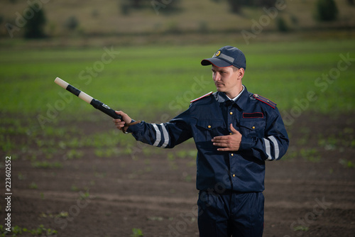 policeman in uniform with a rod in his hand on the background of rural landscape