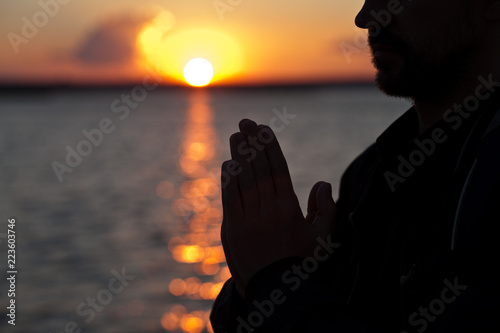 Obraz na plátně The man folded his hands in a prayerful pose against the backdrop of a beautiful