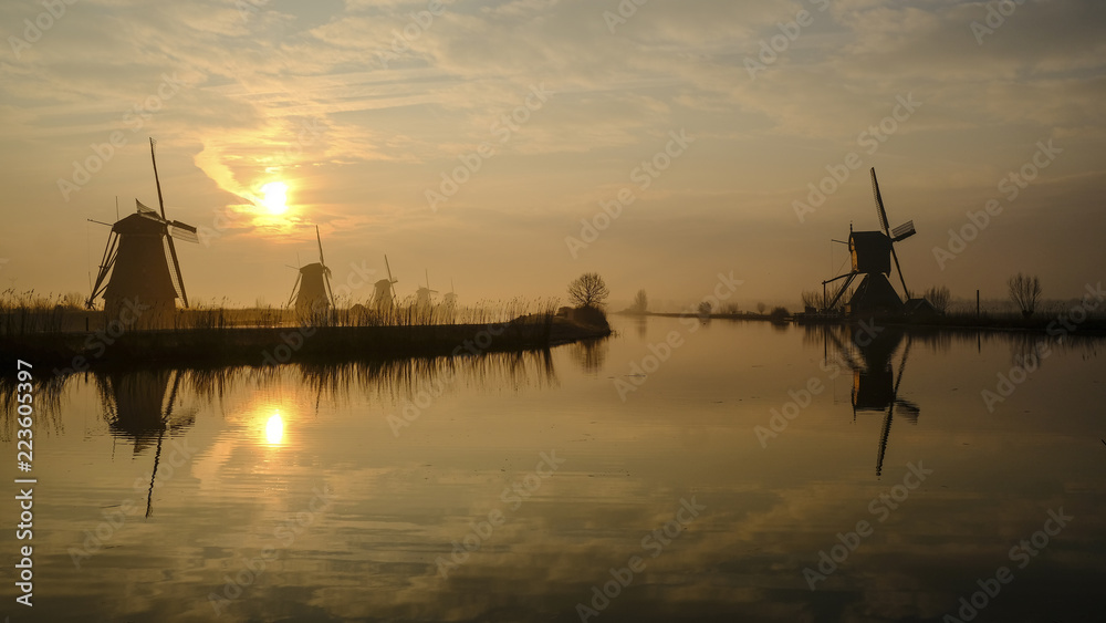 Symmetry view of traditional windmills by river against sky during sunset Symmetry view of traditional windmills by river against sky during sunset