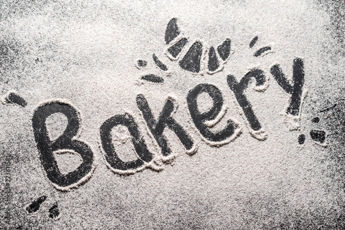 The bakery inscription is made on white wheat flour scattered on a black table. Top view, space for text. Flour ready to knead dough for baking bread, cake or cake