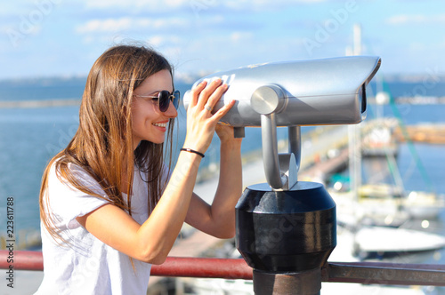 beautiful young woman standing on quay near with telescope and smiling.