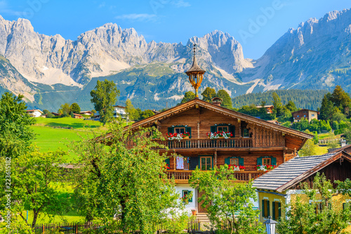 Typical wooden alpine house against Alps mountains background on green meadow in Going am Wilden Kaiser village on sunny summer day, Tyrol, Austria photo