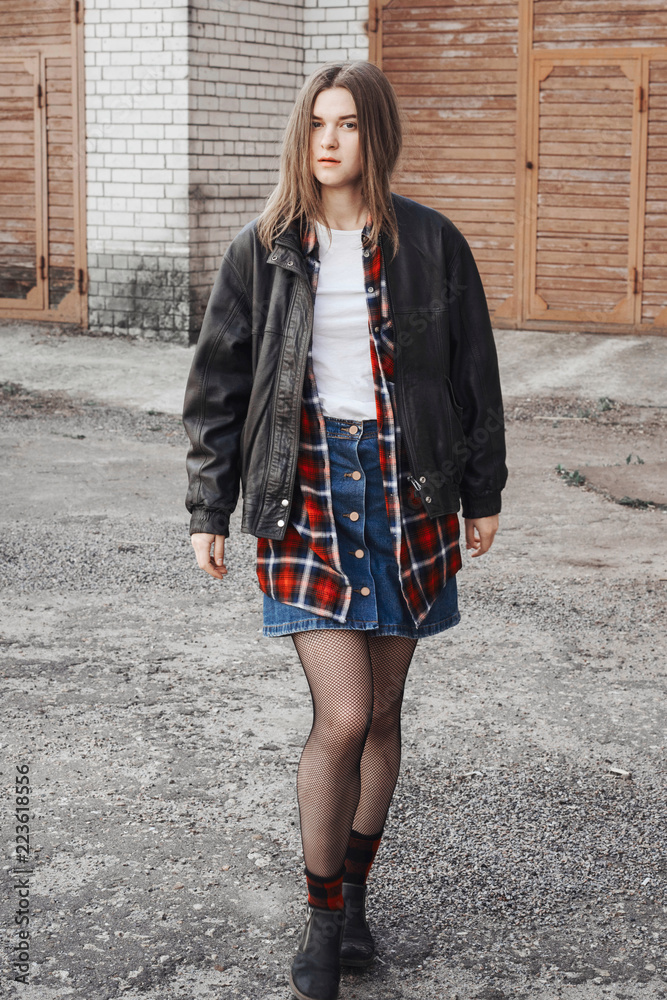 Portrait of a woman in rock, grunge style. Filmed on the street, in the  open space. Dressed in a black leather jacket, shirt in red plaid. Street  style and fashion. Photos