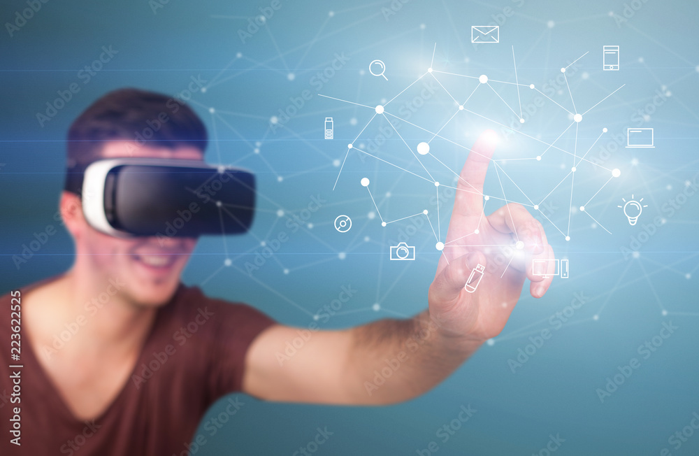 Young impressed man wearing virtual reality goggles with mixed media icons around his finger Young impressed man wearing virtual reality goggles with mixed media icons around his finger