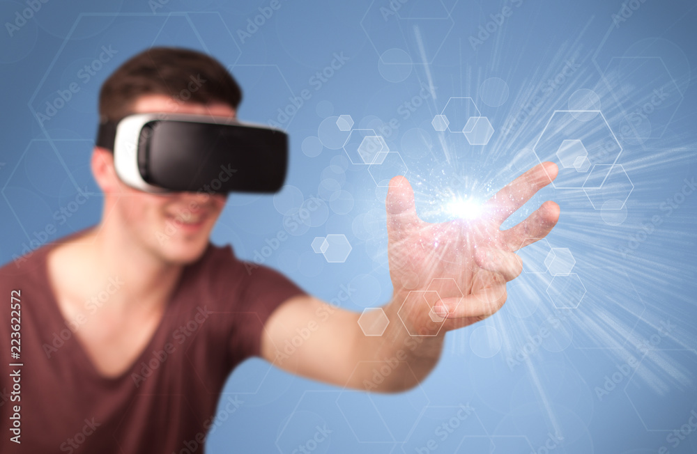 Young impressed man wearing virtual reality goggles with blue hexagons around him Young impressed man wearing virtual reality goggles with blue hexagons around him