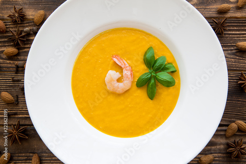 Tasty pumpkin cream soup with shrimps and basil leaves, blended with spice and carrots. Top view.