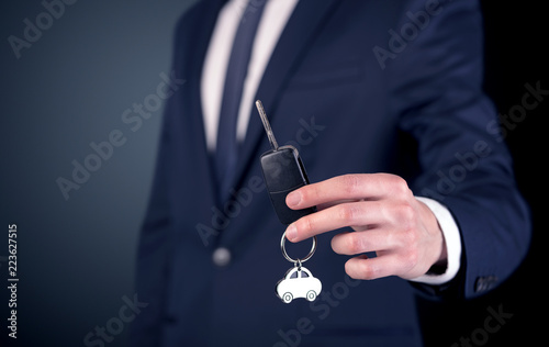 Young businessman hand over keys with empty dark background 