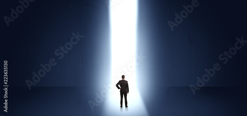 Businessman standing and seeing the light at the end of a big wall  