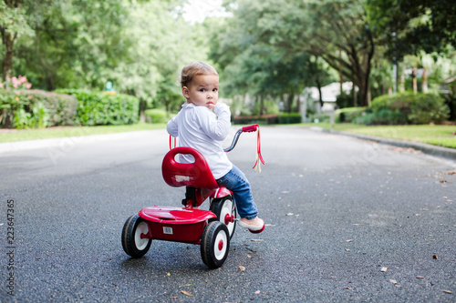 Fotografie Young Child Toddler on Red Tricycle on a Neighborhood Street Looking at Camera