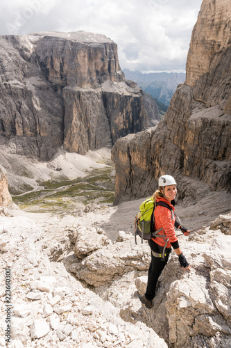 young female mountain climber descending a steep Via Ferrata in the Dolomites of Alta Badia in northern Italy with great landscape behind