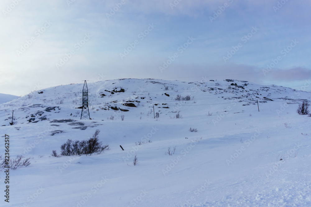 a metal tower of power lines in winter in the boundless tundra in the frost keeps wires with high voltage for a small village