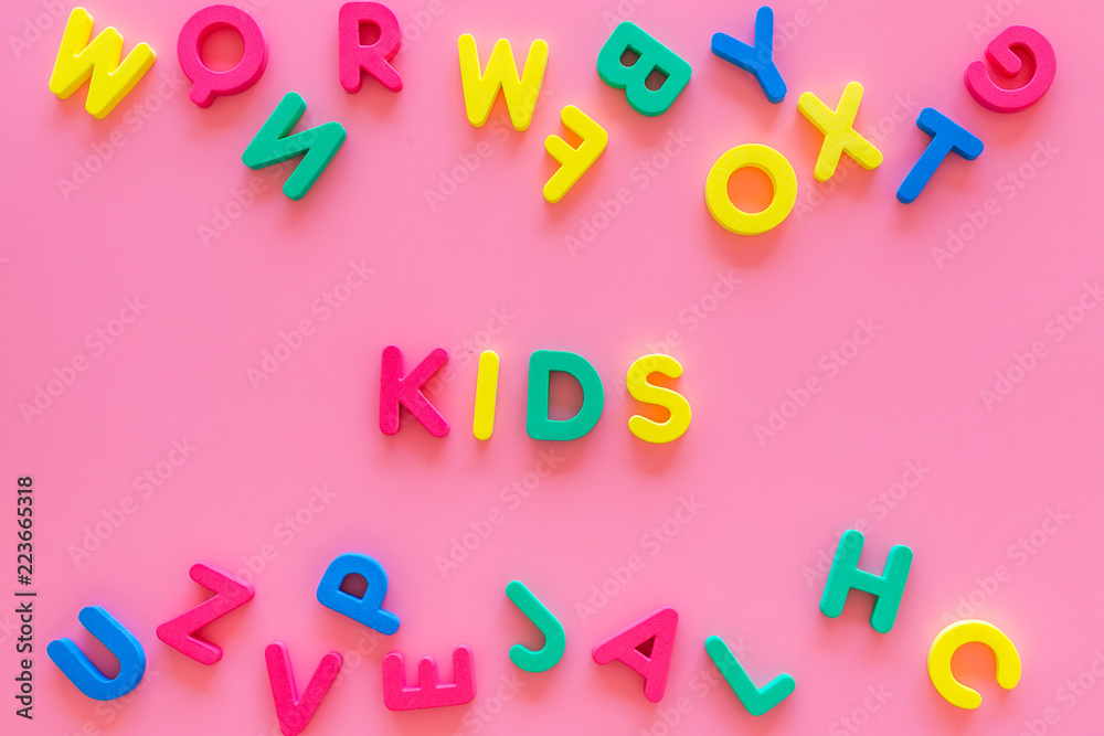 Fototapeta premium Early childhood development concept. Word kids written by plastic letters of toy alphabet on pink background top view copy space