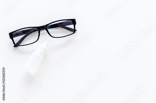 Eye health. Glasses with transparent optical lenses and eye drops on white background top view copy space closeup