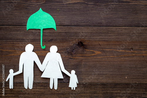 Illustration of social security concept. Financial protection. Family silhouette, cutout under umbrella on dark wooden background top view space for text photo