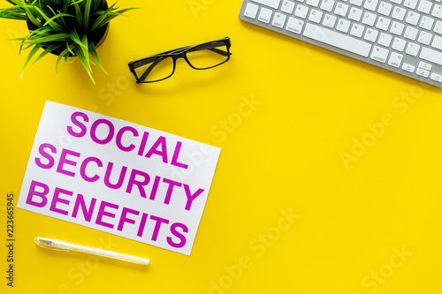 Printed words social security benefits on yellow office desk background with computer keyboard top view copy space