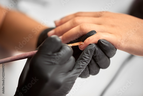 Close-up details shot of beautician hands in black rubber gloves applying with brush transparent gel polish on woman fingernail at beauty salon. Healthcare  beauty cosmetics  spa procedure concept.
