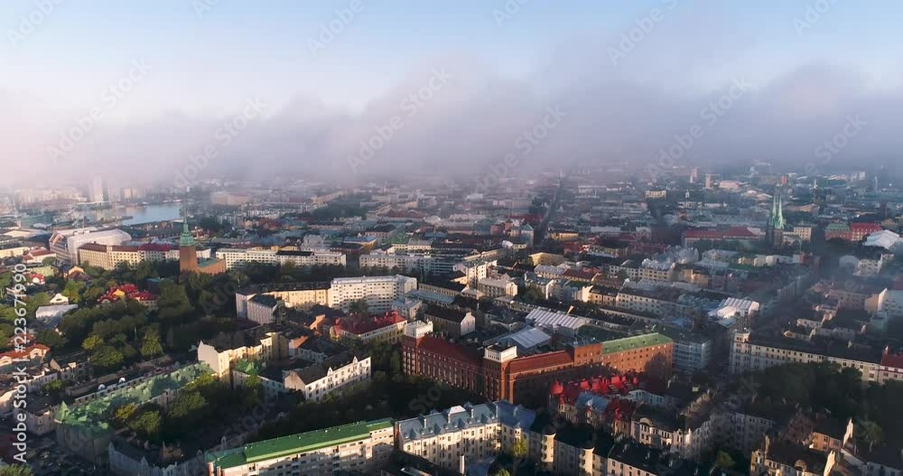 Aerial view of Helsinki capital of Finland. Drone flying backwards on misty clouds during sunny summer morning above city filming old buildings and lots of colorful rooftops. Eira. Ullanlinna.