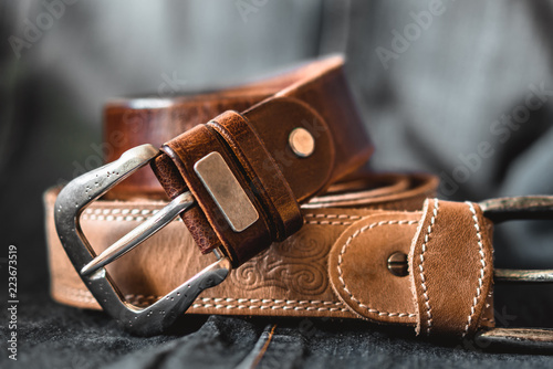 Two brown leather belts on dark background photo