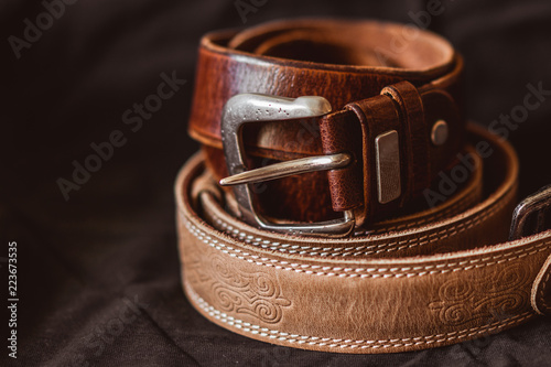 Two brown leather belts on dark background