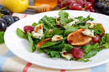 Classic salad with figs, arugula, blue cheese, grapes on a white plate on a wooden table. A delicious vegetarian dish.