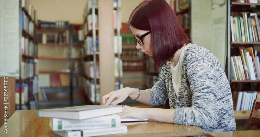 Student girl sitting at a table reading a book in the public library. Student girl sitting at a table reading a book in the public library.